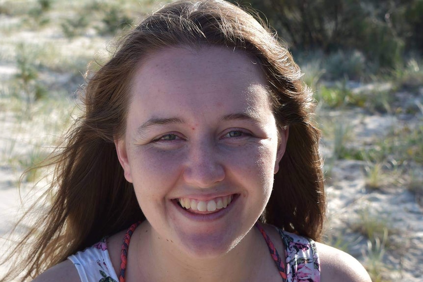 Young woman with brown hair smiling with sand dunes in the background