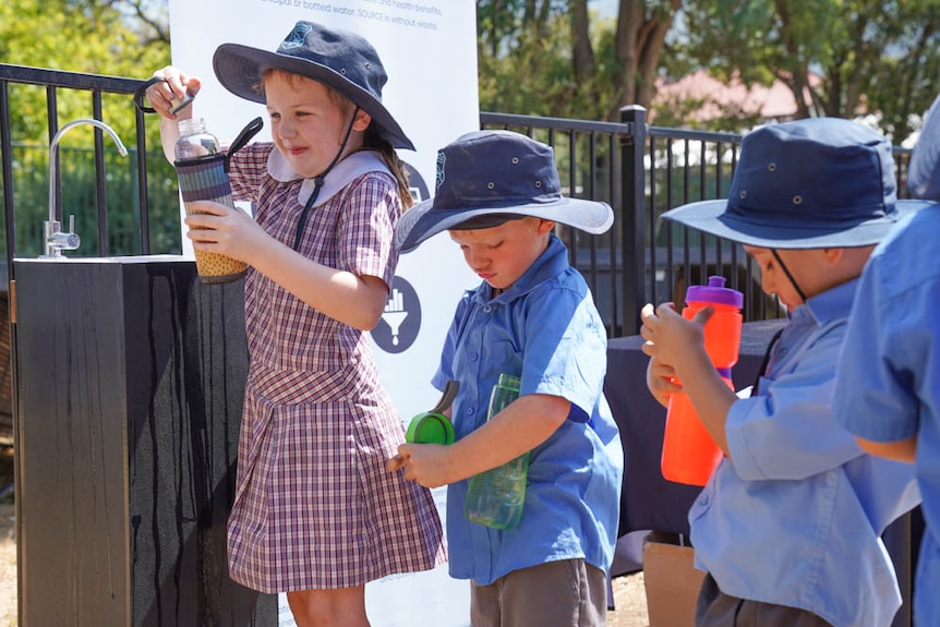 Primary school studnets line up to fill up water bottles from a Source hyrdopanel tap.