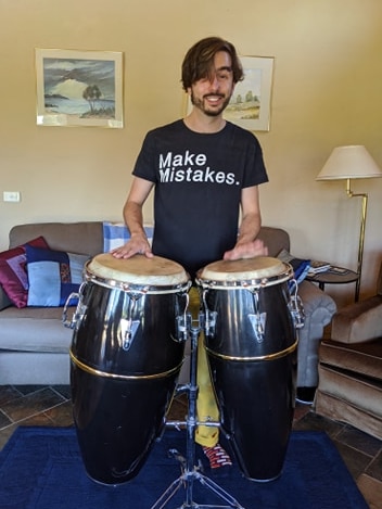 A man stands in a room playing conga drums.