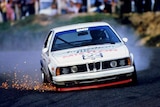 A colour photograph of a BMW race car with sparks coming from its wheels