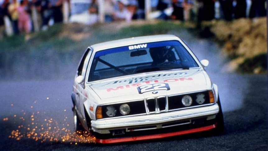 A colour photograph of a BMW race car with sparks coming from its wheels