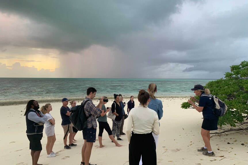 A group of people standing on a Heron Island Beach listening to a guide with reef in the background