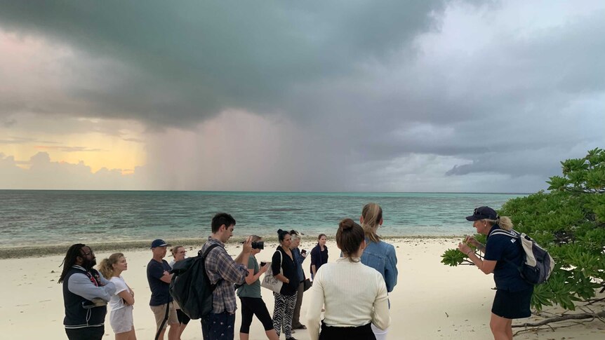 A group of people standing on a Heron Island Beach listening to a guide with reef in the background