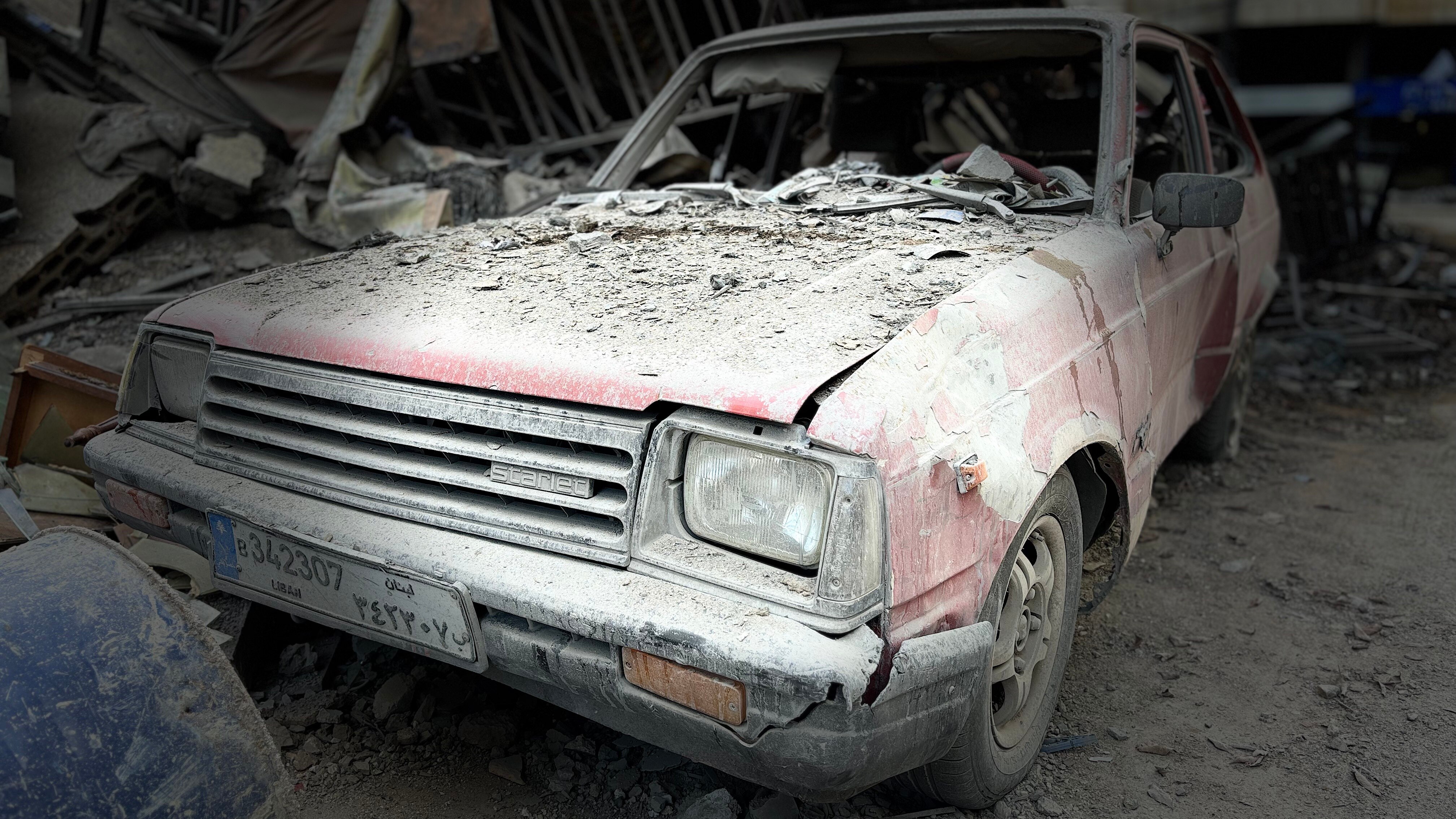 A photo of a car with debris and dust on it. Its windows are smashed.