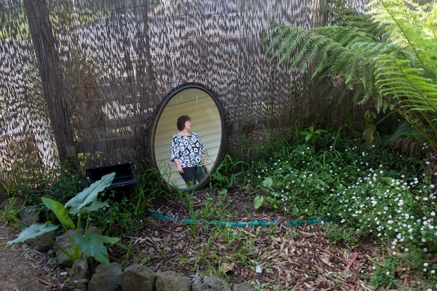 Helen Smith's reflection is caught in a mirror propped in her garden, from which she's removed what she can.