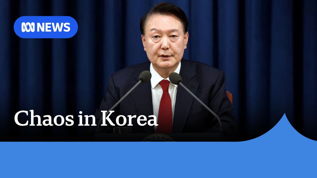 Chaos in Korea: A man in a dark suit and red tie speaking into a pair of microphones.