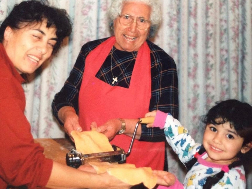 A young girl helps two women make fresh pasta.