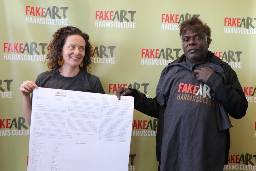 Gabrielle Sullivan and Gabriel Nodea hold up a petition in front of a Fake Art Harms Culture sign.