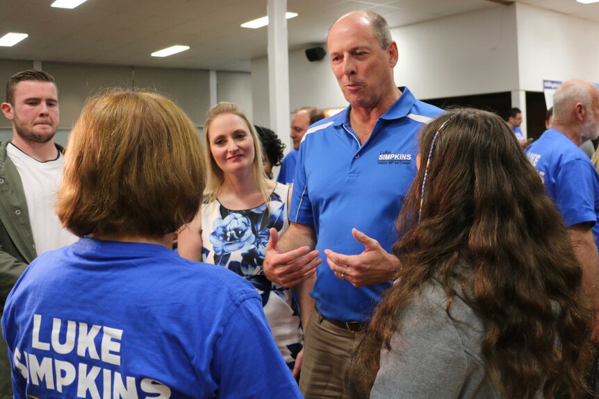 Luke Simpkins speaks to supporters wearing a blue polo shirt emblazoned with his name.