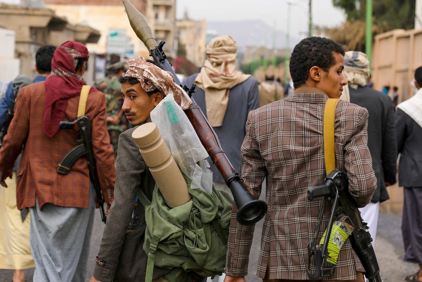 A group of men armed with guns and rocket launchers walk down a street in Yemen