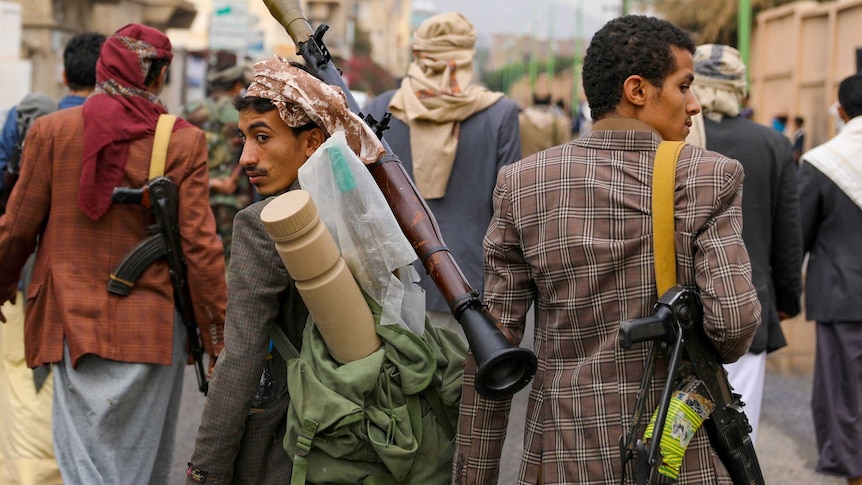 A group of men armed with guns and rocket launchers walk down a street in Yemen