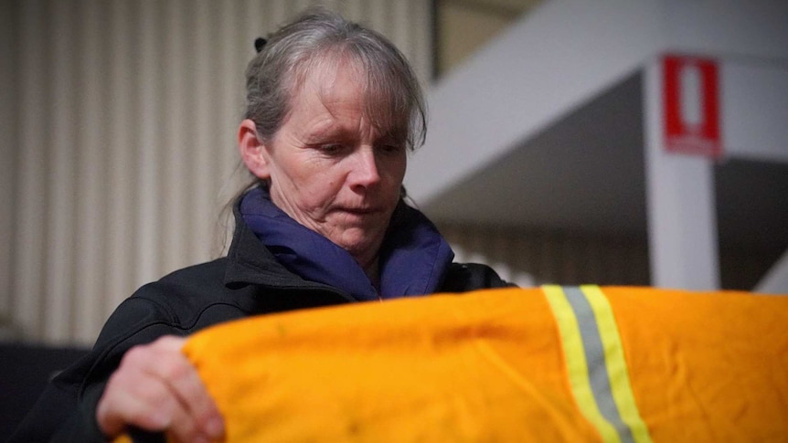 A woman stands and folds RFS pants while standing in a local RFS shed.