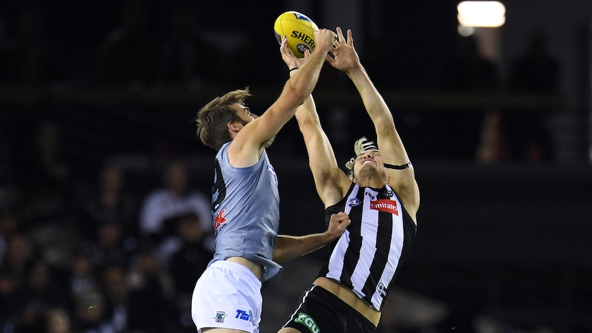 Justin Westhoff and Darcy Moore leap in the air as they contest for the ball with their arms stretched above them.