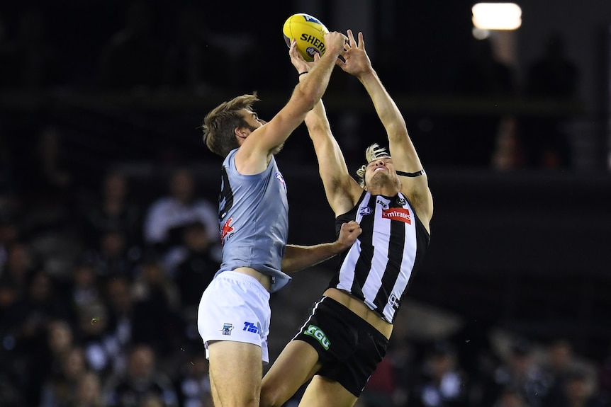 Justin Westhoff and Darcy Moore leap in the air as they contest for the ball with their arms stretched above them.