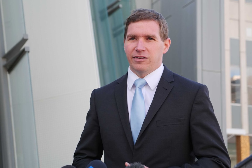 Alistair wears a suit while addressing the media outside the Legislative Assembly.