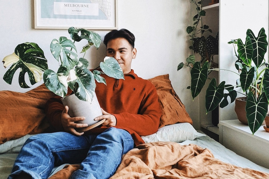 Ben holds his variegated Monstera, sitting in his bedroom.