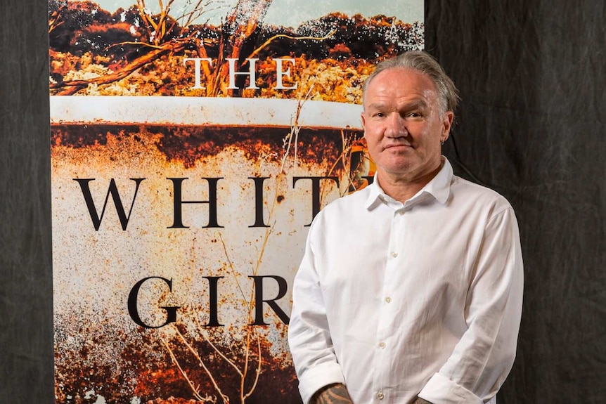 The novelist Tony Birch standing in front of a banner with the cover of his book The White Girl