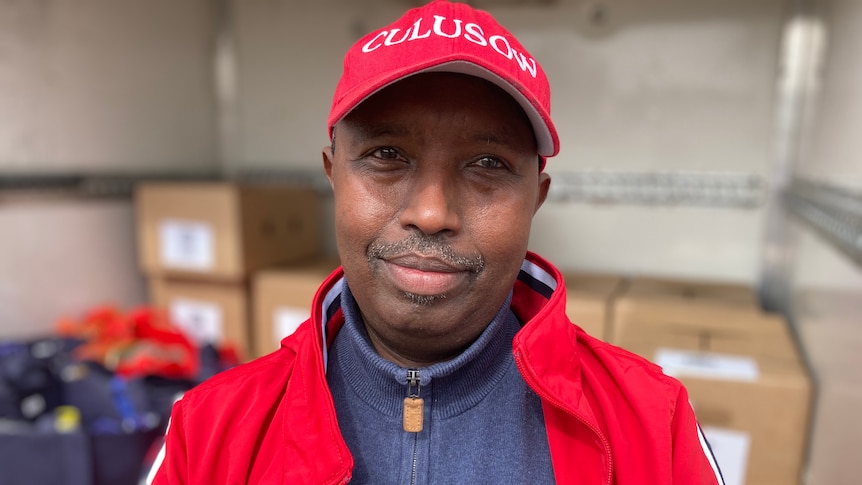 Man wearing a red hat standing behind a truck.