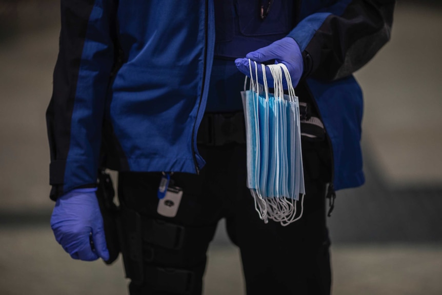 Close up picture of a police officer wearing gloves, with a stack of masks to hand out to commuters