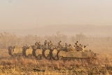 A row of armoured vehicles travels along dry grassland