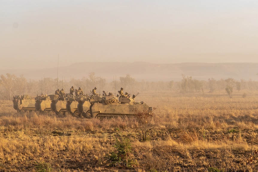 A row of armoured vehicles travels along dry grassland
