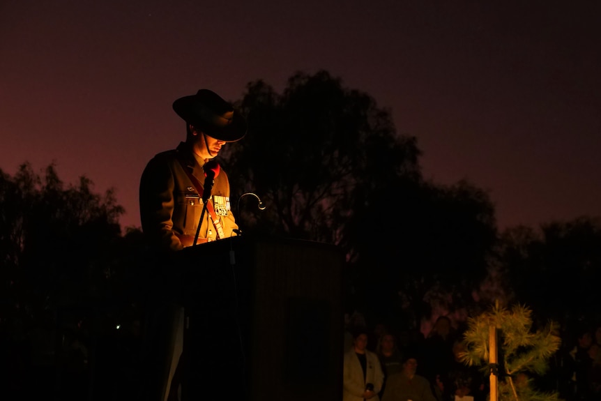 A shadowed picture of an army personnel, in uniform, standing at a lectern.