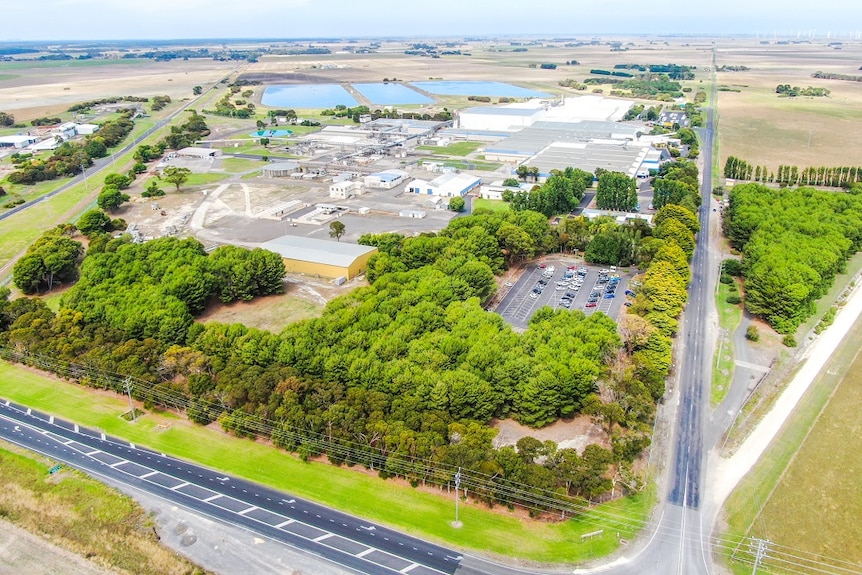 A bird's-eye view of factory roofs, trees and a car park