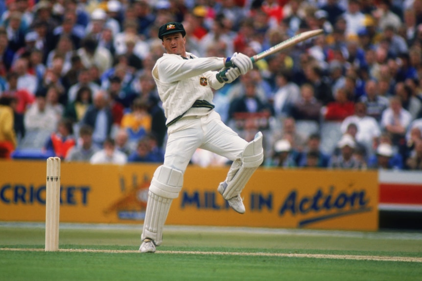 A cricket batter swings his bat through the air while standing on one leg