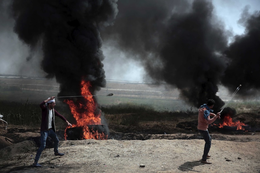 Two men are seen hurling stones amid smoke from burned tires.