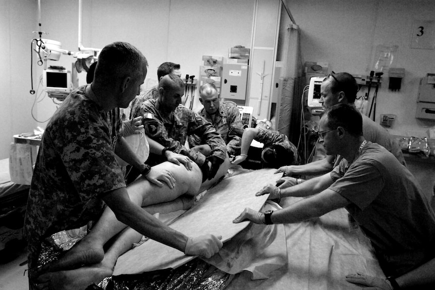 Army medics roll an injured person off a backboard onto a bed