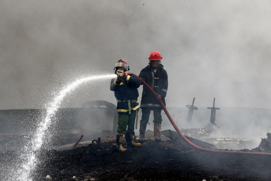 Firefighters spray white foam on a blackened, burned area. 