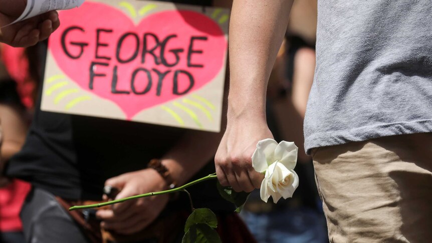 A man holds a white rose as he stands outside during a memorial service for George Floyd