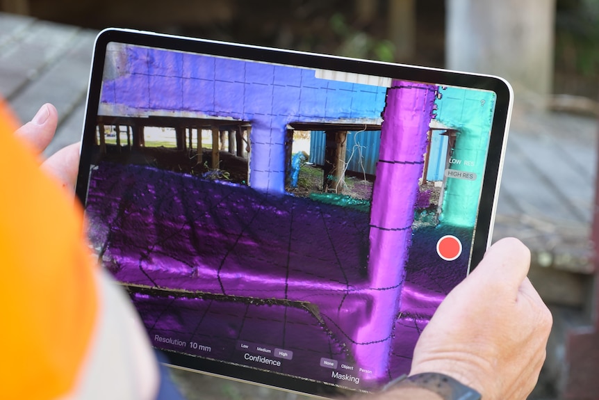 a man holds an ipad pointed at the exterior of a building. A purple image of the building is generated on the screen