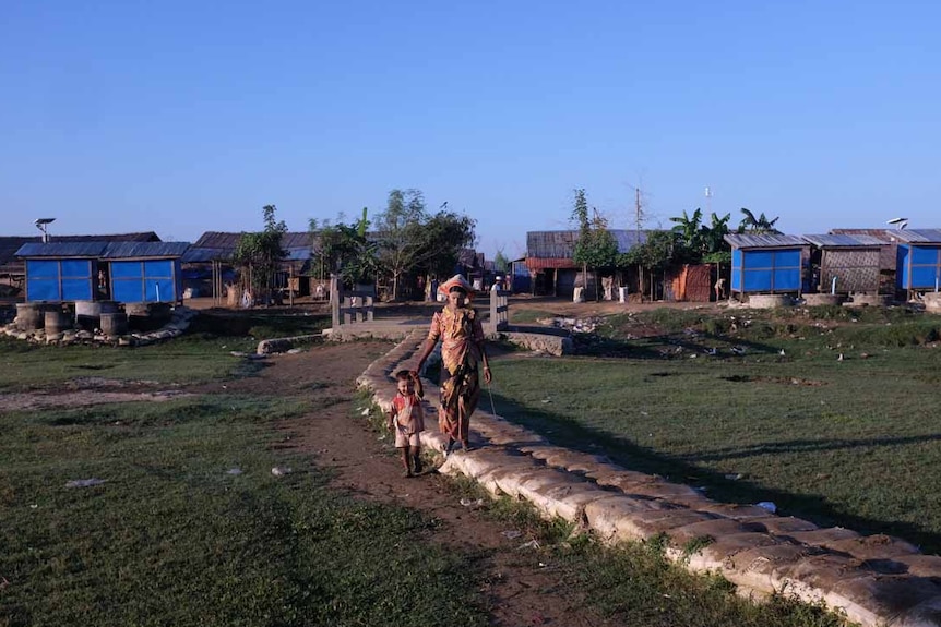 A woman and child walk between two of the better-served camps on the outskirts of the state capital of Sittwe.