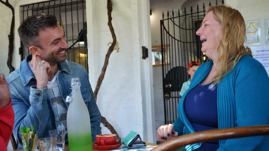Greens candidates Rob Simms and Tammy Frank looking at each other and laughing at a cafe.