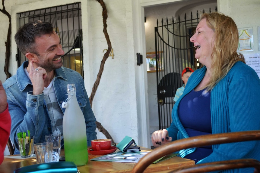 Greens candidates Rob Simms and Tammy Frank looking at each other and laughing at a cafe.