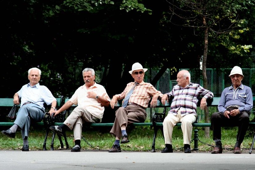 Elderly men sit on a park bench and enjoy the sun.