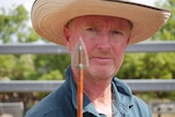 A man in a cowboy hat stands looking at arrow.