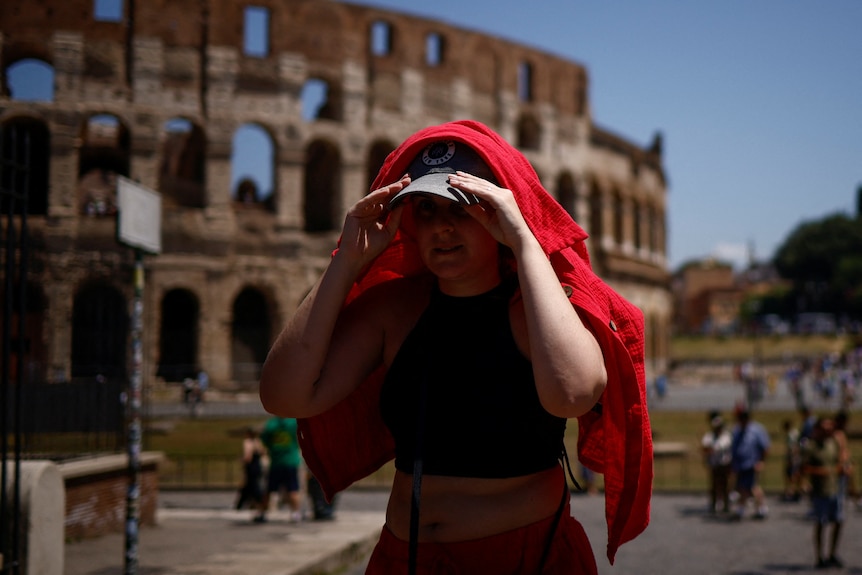 A woman shelters from the sun with a shirt near the Colosseum during a heatwave.