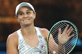 An Australian female tennis player claps her racquet as she applauds the crowd.