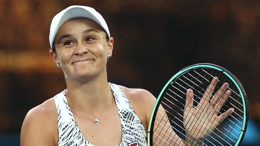 An Australian female tennis player claps her racquet as she applauds the crowd.