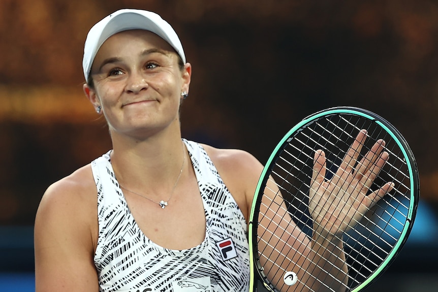 An Australian female tennis player claps her racquet as she applauds the crowd.