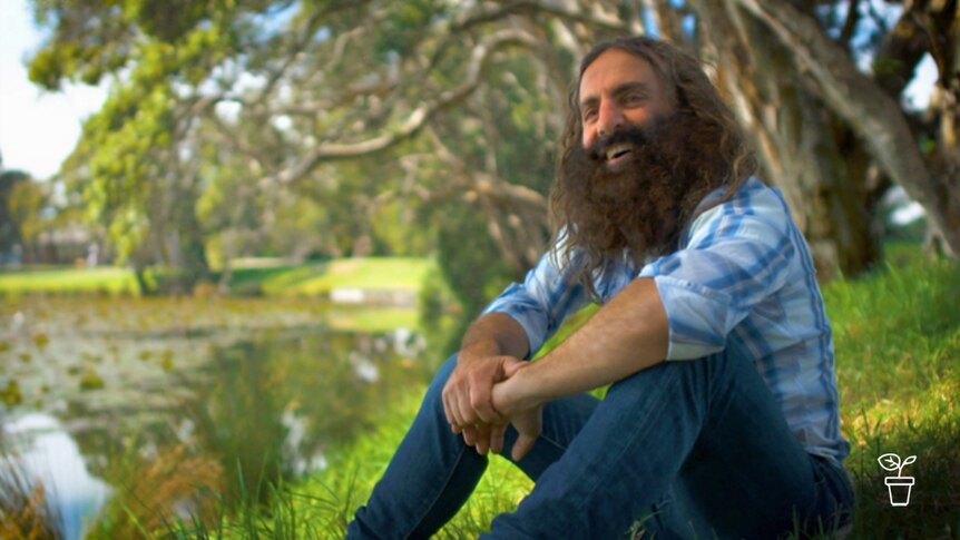 Man with beard smiling and sitting underneath a tree by the river