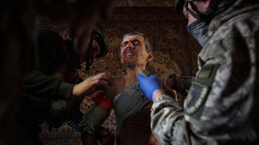 Ukrainian soldiers and police officers provide first aid to a local resident as he winces in pain.