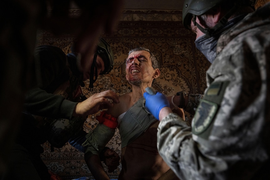 Ukrainian soldiers and police officers provide first aid to a local resident as he winces in pain.