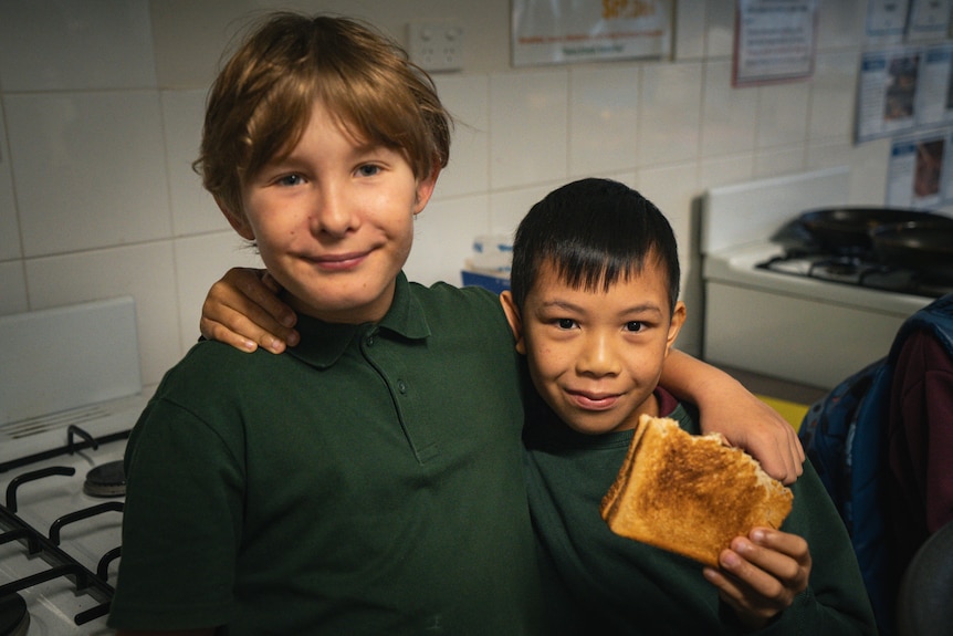 Two young boys in green uniforms with arms wrapped around each other smile, one holds toast
