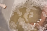 A bath tub filled with brown water with a child's foot in the picture.