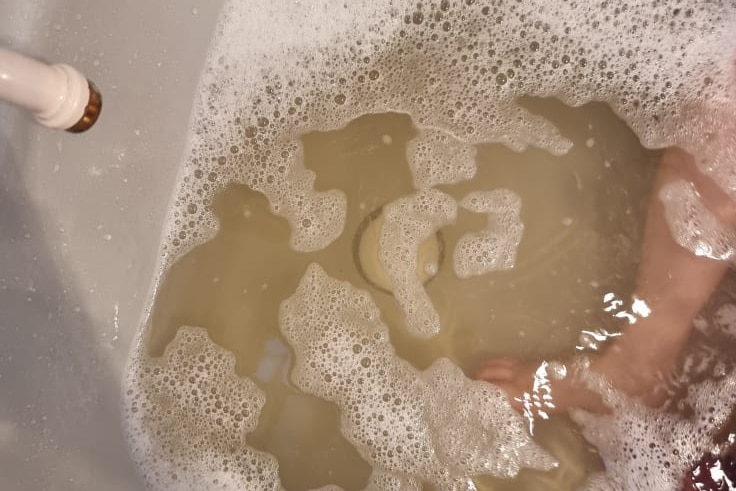 A bathtub filled with brown water with a baby foot in the picture.