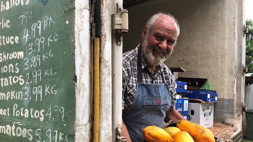 A smiling, bearded man sits in the back of the fruit truck he's driven to outback towns for the past 30 years.