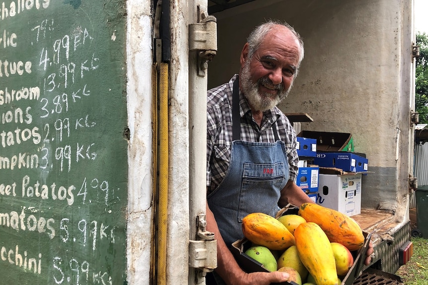 A smiling, bearded man sits in the back of the fruit truck he's driven to outback towns for the past 30 years.